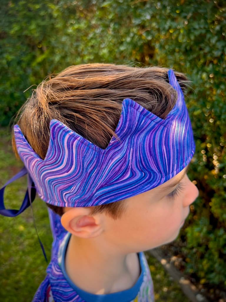 Child wearing a purple handmade birthday crown in a leafy garden