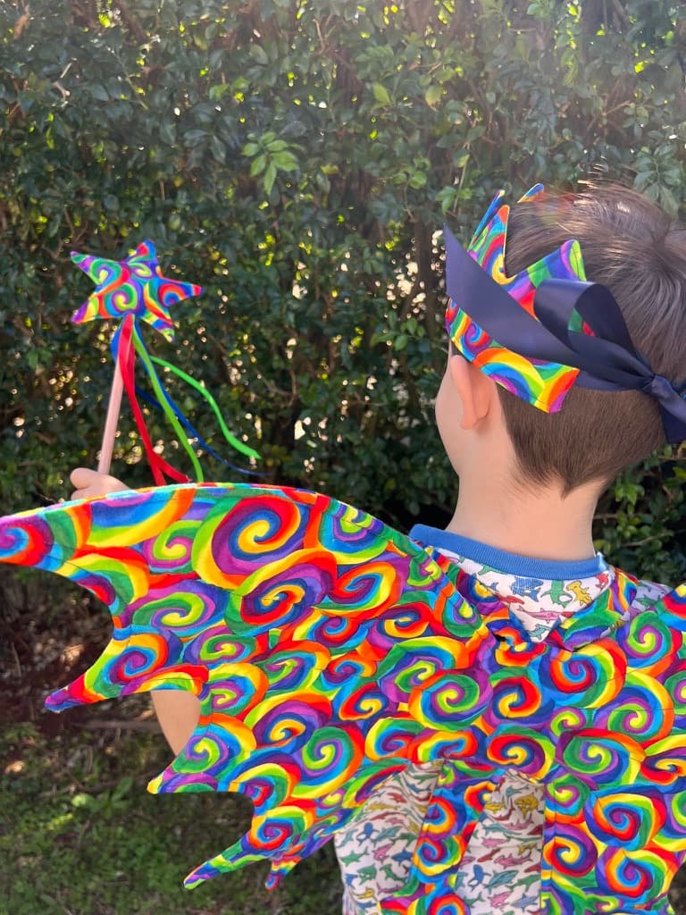 Child in rainbow dragon wings holding a matching star wand and wearing a crown