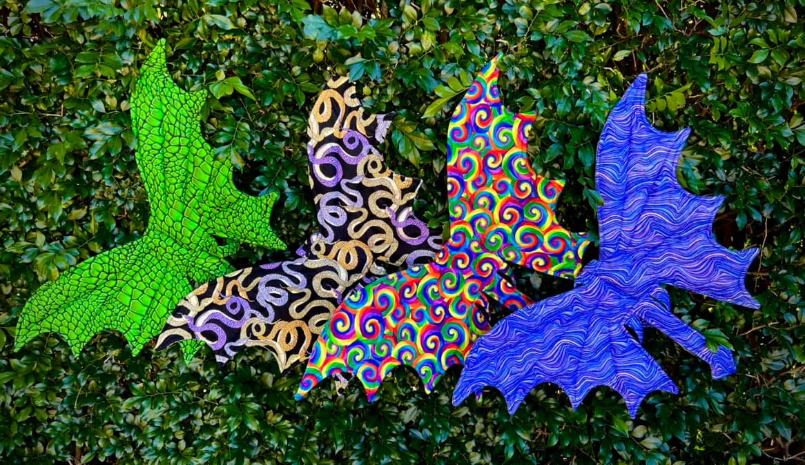 Four handmade dragon wing designs arranged together in woodland foliage