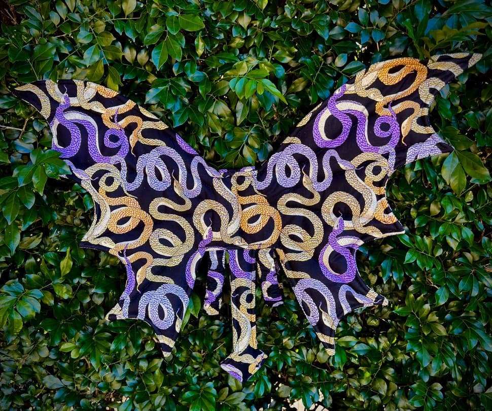 Gilded Serpents handmade dragon wings displayed against deep green leaves